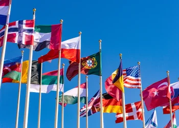 National flags of multiple countries flying against a clear blue sky