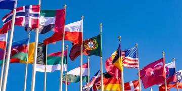 National flags of multiple countries flying against a clear blue sky