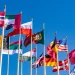 National flags of multiple countries flying against a clear blue sky