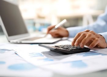 Person using a calculator and laptop to review student loan and financial documents.