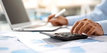 Person using a calculator and laptop to review student loan and financial documents.