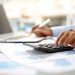 Person using a calculator and laptop to review student loan and financial documents.