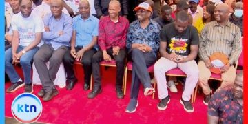 Kenyan political leaders seated together at a Linda Mwananchi rally event with supporters in the background