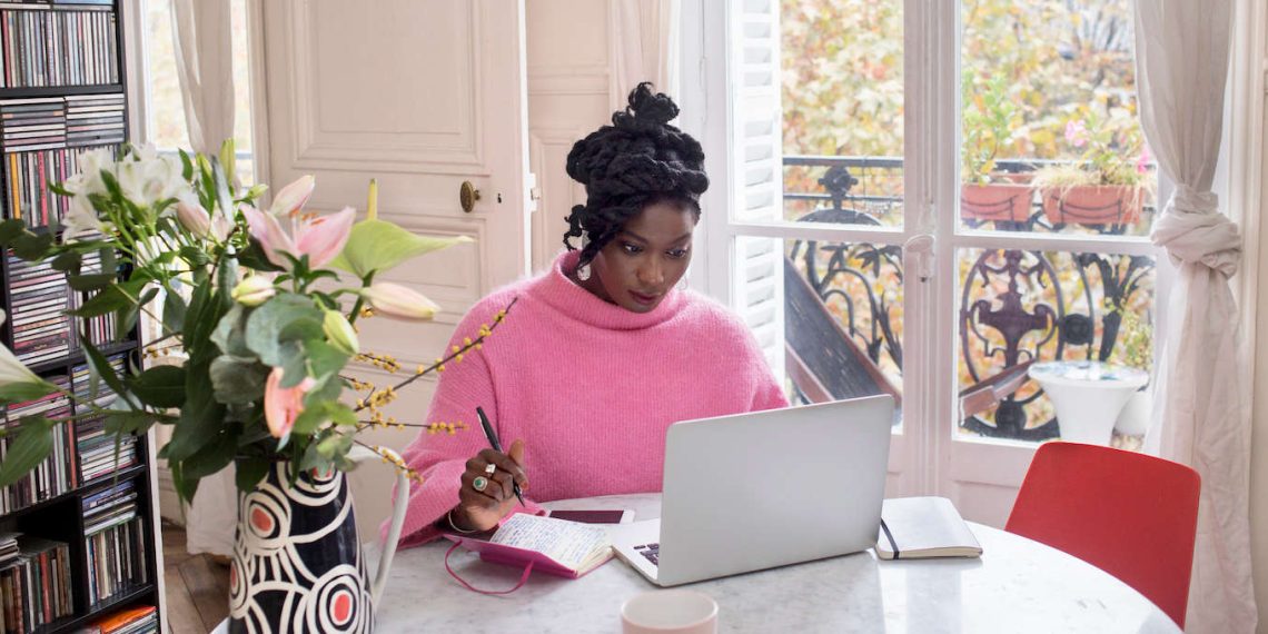 Confident African woman working on laptop using AI tools for side hustle at a bright home office setup in 2026