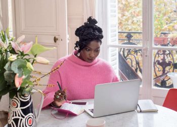 Confident African woman working on laptop using AI tools for side hustle at a bright home office setup in 2026