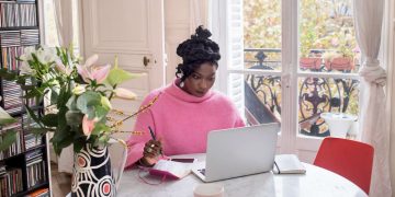 Confident African woman working on laptop using AI tools for side hustle at a bright home office setup in 2026