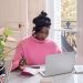 Confident African woman working on laptop using AI tools for side hustle at a bright home office setup in 2026
