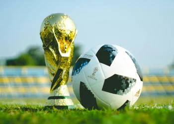 alt="FIFA World Cup Trophy and official match ball on grass in stadium"